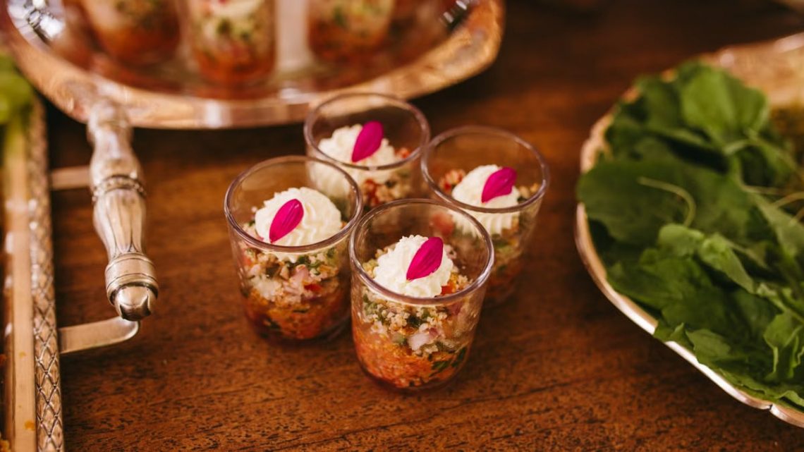 Delightful layered appetizers in glass cups beautifully presented with fresh greens on a wooden table.