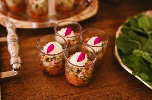 Delightful layered appetizers in glass cups beautifully presented with fresh greens on a wooden table.