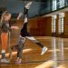 Two young girls practicing gymnastics in a sunlit gymnasium, showcasing teamwork and skill.